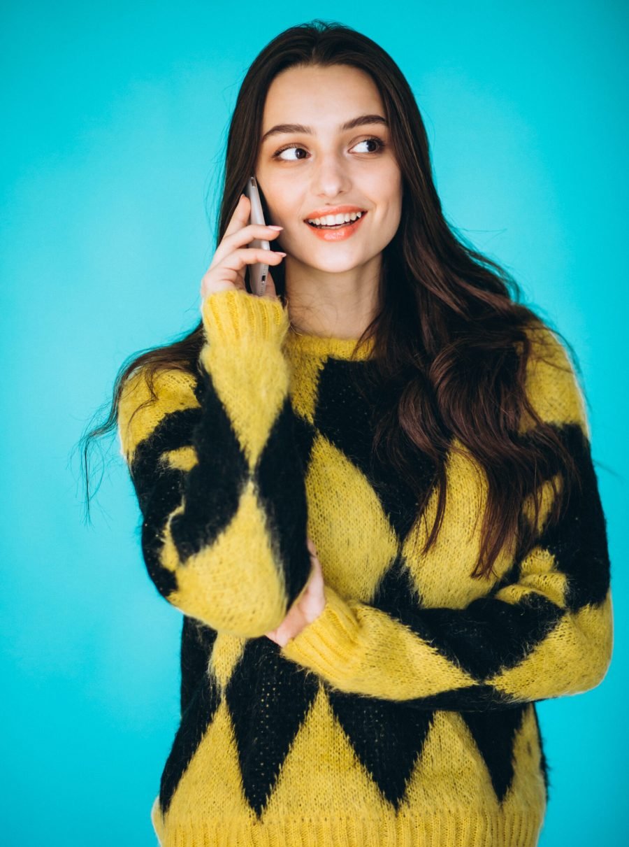 Young woman in a warm sweater using phone in studio